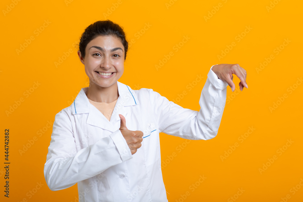 Portrait of indian doctor woman in white medical gown holding fingers template vaccine covid-19 or other medical stuff isolated on yellow background. Portrait of indian doctor woman in white medical gown holding fingers template vaccine covid-19 or other medical stuff isolated on yellow background.
