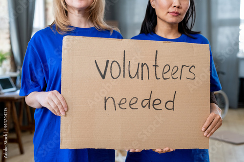 Two intercultural females holding poster announcing need of volunteers