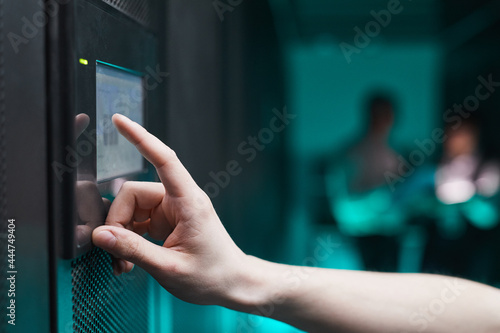 Side view close up of unrecognizable man operating server cabinet via digital control panel in data center, copy space