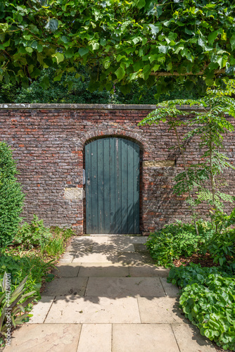 Fototapeta Naklejka Na Ścianę i Meble -  A green walled garden door in a red brick wall with a slabed footpath