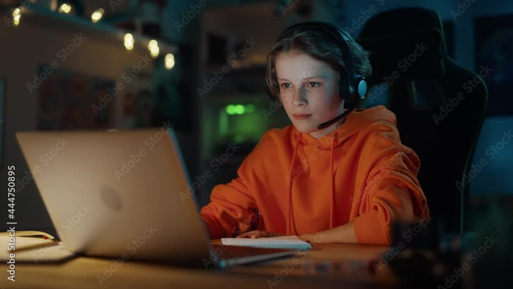 Smart Young Boy in Headphones Attending Online Class on Laptop Computer in Cozy Dark Room at Home. Happy Teenager Browsing Educational Research Online, Writing in Notebook, Studying School Homework. Smart Young Boy in Headphones Attending Online Class on Laptop Computer in Cozy Dark Room at Home. Happy Teenager Browsing Educational Research Online, Writing in Notebook, Studying School Homework.