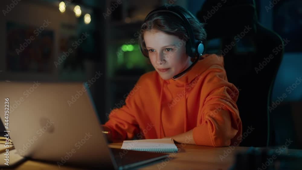 Smart Young Boy in Headphones Attending Online Class on Laptop Computer in Cozy Dark Room at Home. Happy Teenager Browsing Educational Research Online, Writing in Notebook, Studying School Homework. Smart Young Boy in Headphones Attending Online Class on Laptop Computer in Cozy Dark Room at Home. Happy Teenager Browsing Educational Research Online, Writing in Notebook, Studying School Homework.