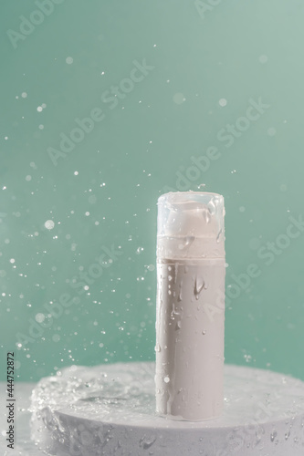 Cosmetic bottle with water splashes on a green background.