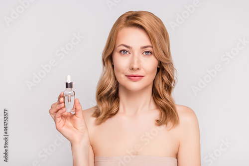 Portrait of attractive woman holding in hand serum bottle advert new bio product isolated over grey pastel color background