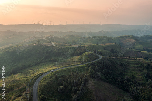 Aerial view of Curved highway on green hill and wind turbine on peak at sunset in countryside