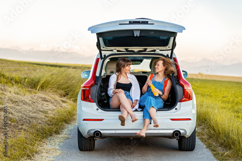 Mother and teenager daughter enjoying their road trip in countryside sitting in open car boot. Local traveling, summer holidays lifestyle. © Tetiana Soares