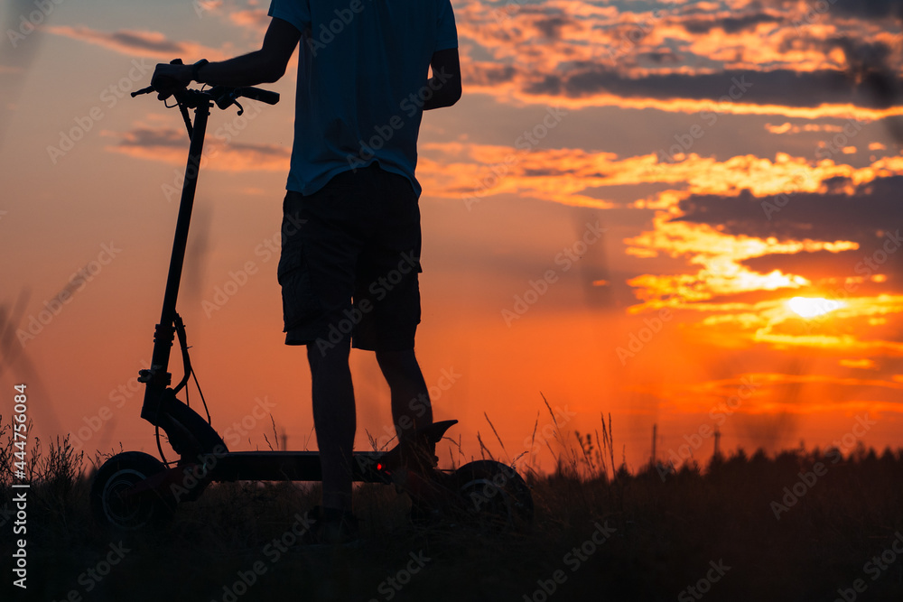 Obraz premium The feeling and concept of freedom. Riding an electric scooter. A young man on a scooter enjoys the sunset