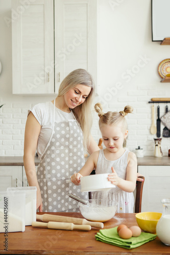 Cute little girl helps mom bake cookies in the kitchen