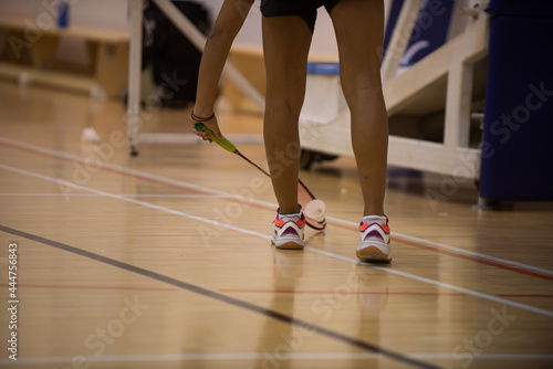 Female badminton player picks up a shuttlecock placed on wooden court while playing a match in a tournament.