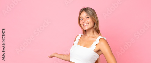 blonde pretty woman feeling happy and cheerful, smiling and welcoming you, inviting you in with a friendly gesture photo