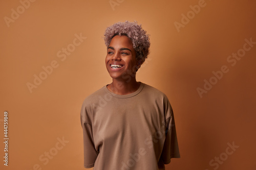 Portrait of emotional beautiful African American woman laughing looking to the side and standing against beige background. People success youth millennials and happiness concept