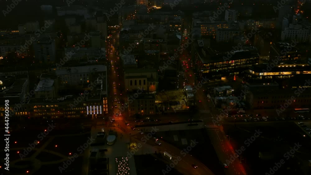 Drone shot at the metropolis at dusk in the winter city of Warsaw, Poland. The camera moves back showing the streets of the city and rises to skyscrapers with night lighting and a beautiful orange sky Drone shot at the metropolis at dusk in the winter city of Warsaw, Poland. The camera moves back showing the streets of the city and rises to skyscrapers with night lighting and a beautiful orange sky