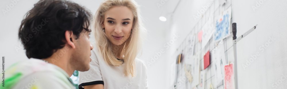 young designer talking to blonde colleague near drawings on wall, banner young designer talking to blonde colleague near drawings on wall, banner