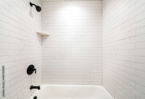 Slika na platnu Alcove bathtub with black plumbing fixtures and white subway tiles wall surround