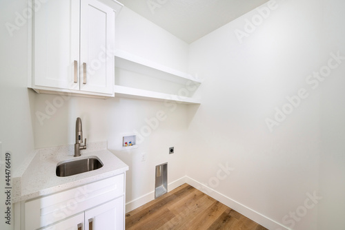 Empty white laundry room with top storage, laundry connections and dryer vent on the wall