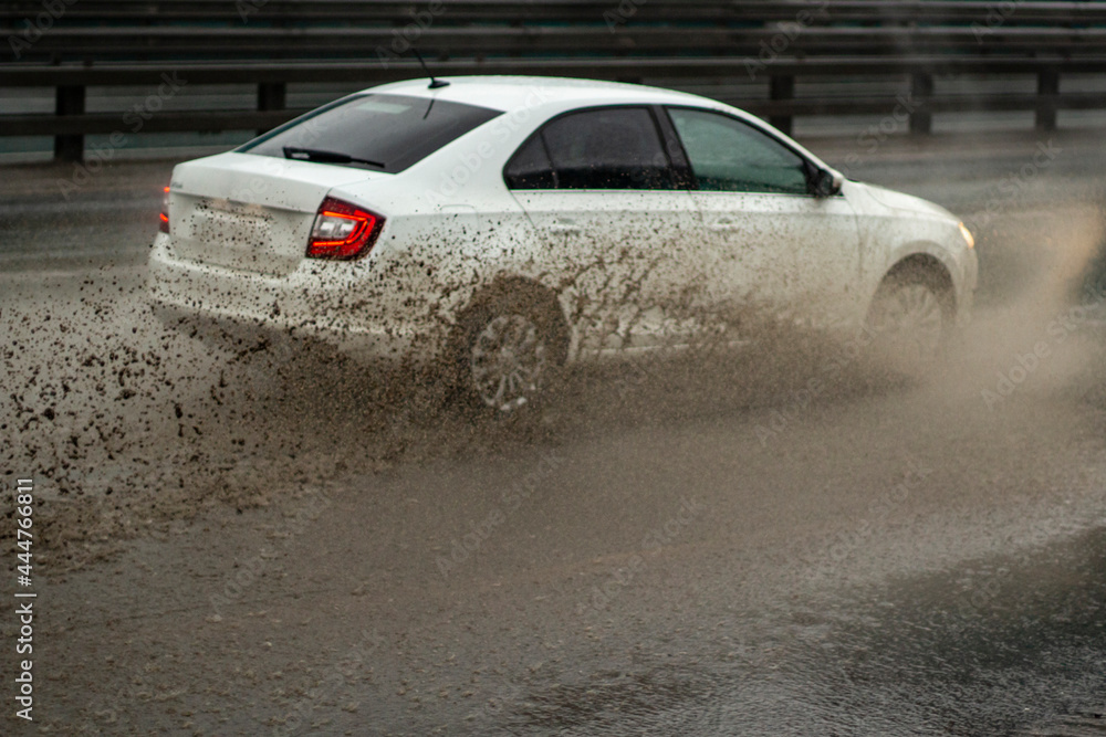The car is driving through a puddle. Splashes from a puddle on the road.