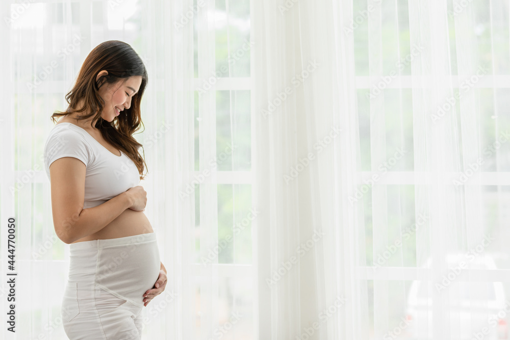 Happy Pregnant Woman standing in front of windows and stroking her big belly with love at cozy home,Pregnancy of young woman enjoy with future life relax with love,Motherhood and Pregnant Concept Happy Pregnant Woman standing in front of windows and stroking her big belly with love at cozy home,Pregnancy of young woman enjoy with future life relax with love,Motherhood and Pregnant Concept