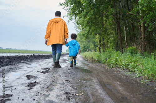 Father and son wearing raincoats walking through the swampy road