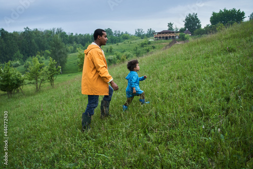 Boy walking through the green hills with his father while enjoying of the rainy weather