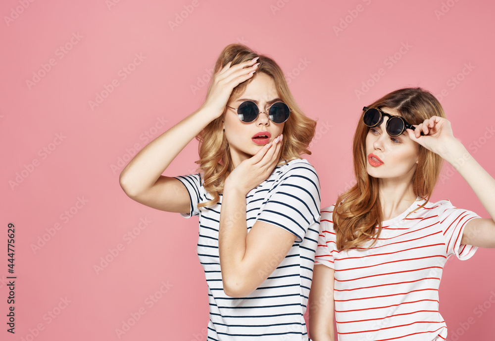 two girlfriends stand side by side in striped t-shirts glasses fashion summer pink background two girlfriends stand side by side in striped t-shirts glasses fashion summer pink background
