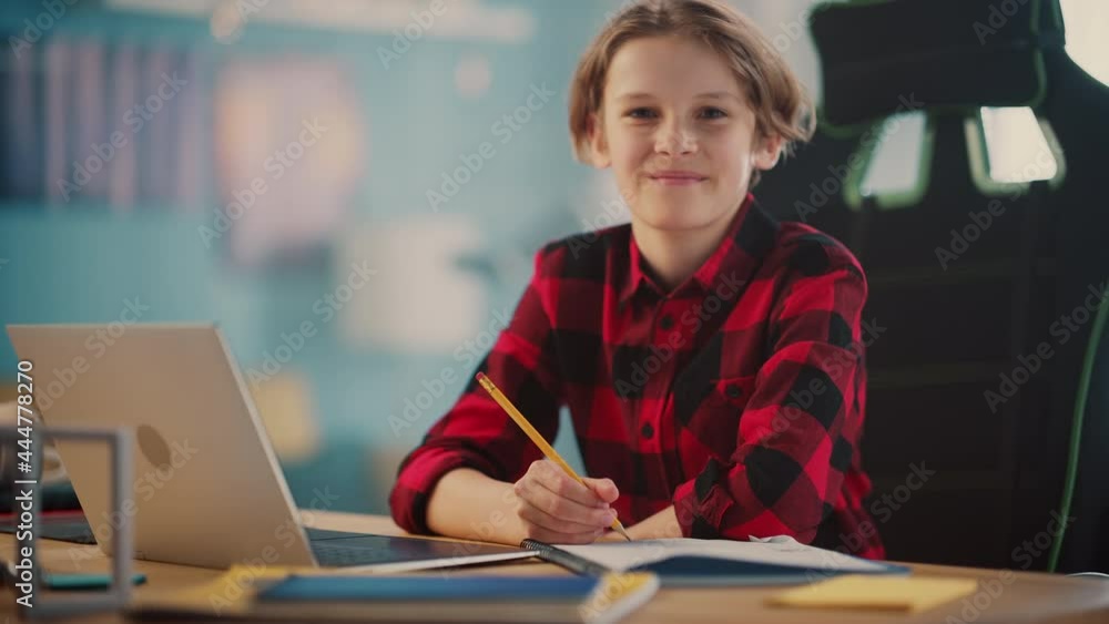 Portrait of a Smart Young Boy Doing Homework on a Laptop Computer in Cozy Room at Home. Teenager is Happy, Looks at the Camera and Smiles. Home Education Concept. Portrait of a Smart Young Boy Doing Homework on a Laptop Computer in Cozy Room at Home. Teenager is Happy, Looks at the Camera and Smiles. Home Education Concept.