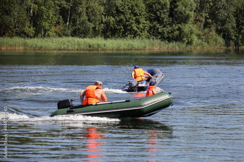 Two inflatable motor boats with outboard motors and people in orange lifejackets fast floating on the water on green forest background , active recreation on the water at Sunnny summer day