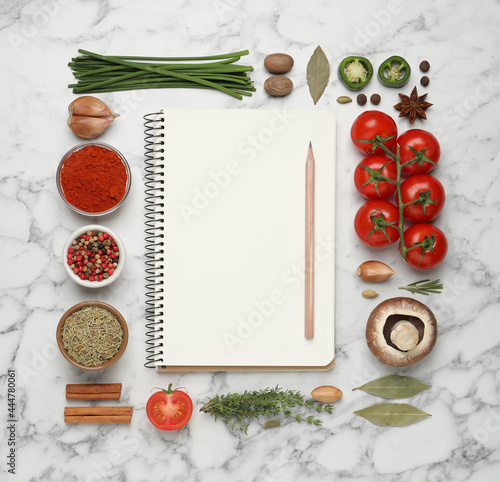 Open recipe book and different ingredients on white marble table, flat lay. Space for text