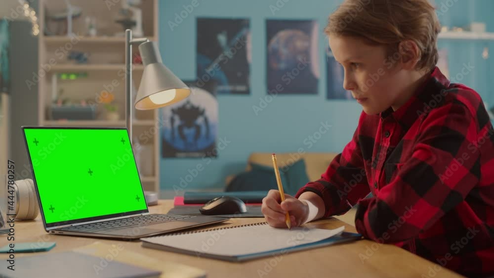 Smart Young Boy in Headphones Attending Online Class on Laptop Computer with Green Screen at Home. Happy Teenager Browsing Educational Research Online, Writing in Notebook, Studying School Homework. Smart Young Boy in Headphones Attending Online Class on Laptop Computer with Green Screen at Home. Happy Teenager Browsing Educational Research Online, Writing in Notebook, Studying School Homework.