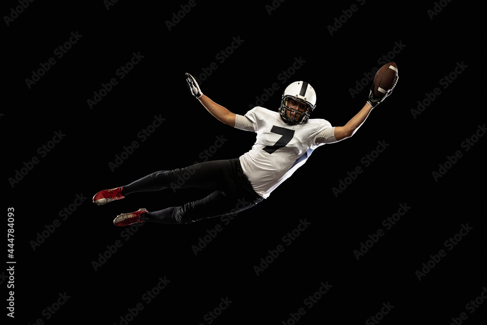 Portrait young American football player, athlete in black white sports uniform training isolated on dark studio background. Concept of professional sport, championship, competition.
