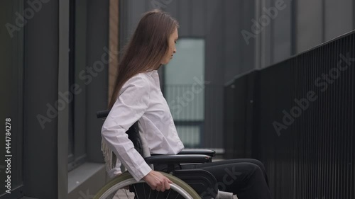 Young paraplegic woman rolling wheelchair outdoors leaving. Portrait of slim beautiful disabled Caucasian elegant businesswoman riding away in slow motion. Disability and business concept photo