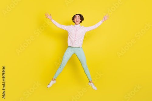 Full size photo of cheerful funky young woman jump up air star shape raise hands isolated on bright yellow color background