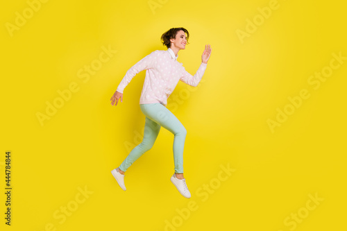 Full size profile side photo of happy girl run hurry sale empty space jump air wear green pants isolated on yellow color background