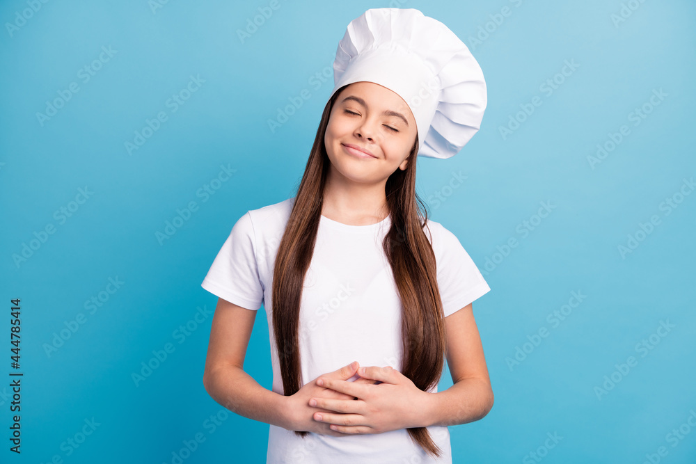 Photo of joyful happy cheerful little girl hold hands stomach good meal isolated on blue color background Photo of joyful happy cheerful little girl hold hands stomach good meal isolated on blue color background