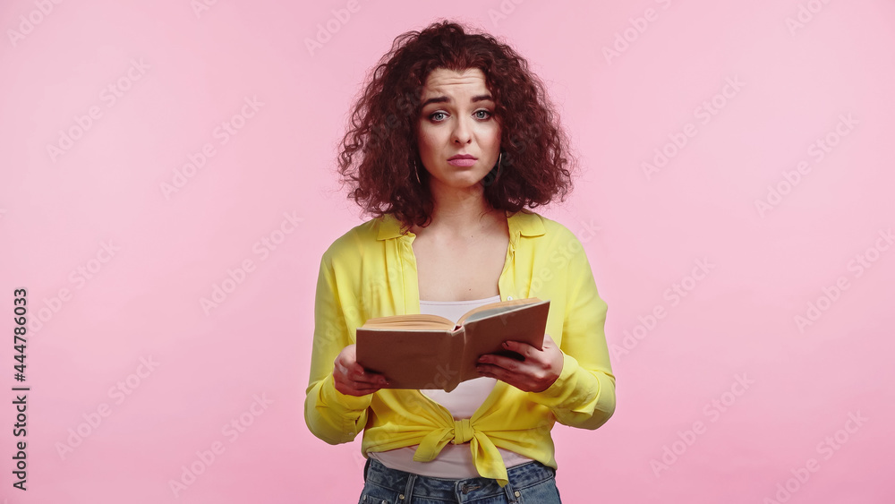 curly and sad student holding book isolated on pink curly and sad student holding book isolated on pink