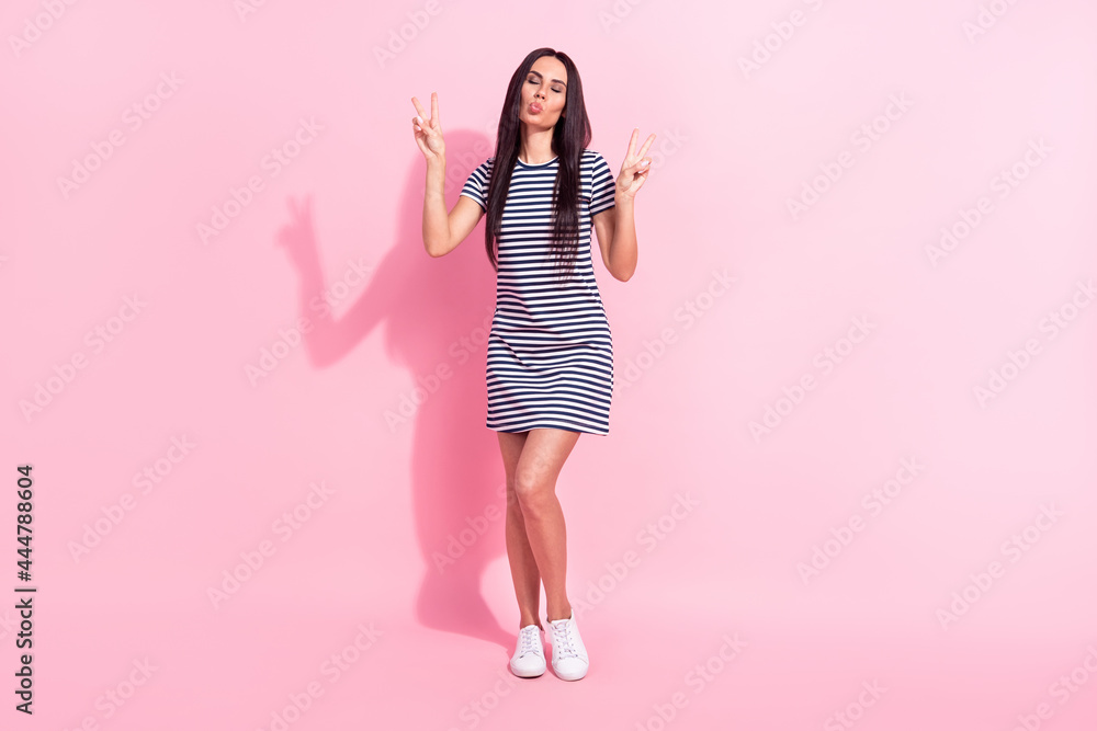 Full length body size view of lovely dreamy woman sending air kiss showing double v-sign isolated over pink pastel color background Full length body size view of lovely dreamy woman sending air kiss showing double v-sign isolated over pink pastel color background