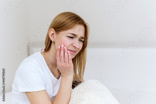 Close-up of a young woman suffering from toothache while sitting in bed. Close-up photo of a man touching her cheek and twisting her lips due to tooth pain
