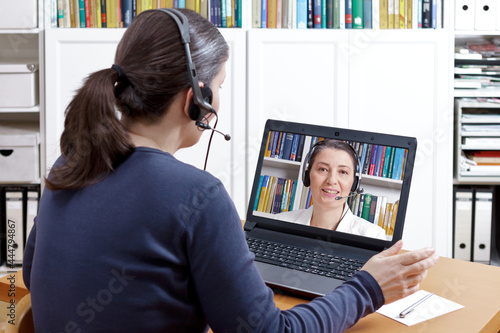 Woman with headset at her desk in front of her laptop having an online call with her therapist, text space photo