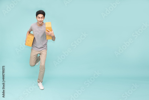 Young Asian delivery man running and holding parcel box isolated on green background