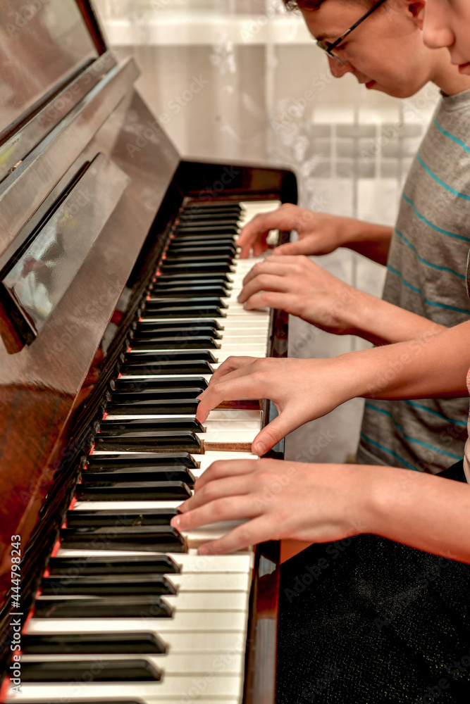 Fototapeta premium A girl and a guy play the piano in four hands. Rehearsal and training at a music school.