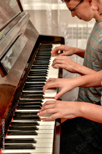 A girl and a guy play the piano in four hands. Rehearsal and training at a music school.
