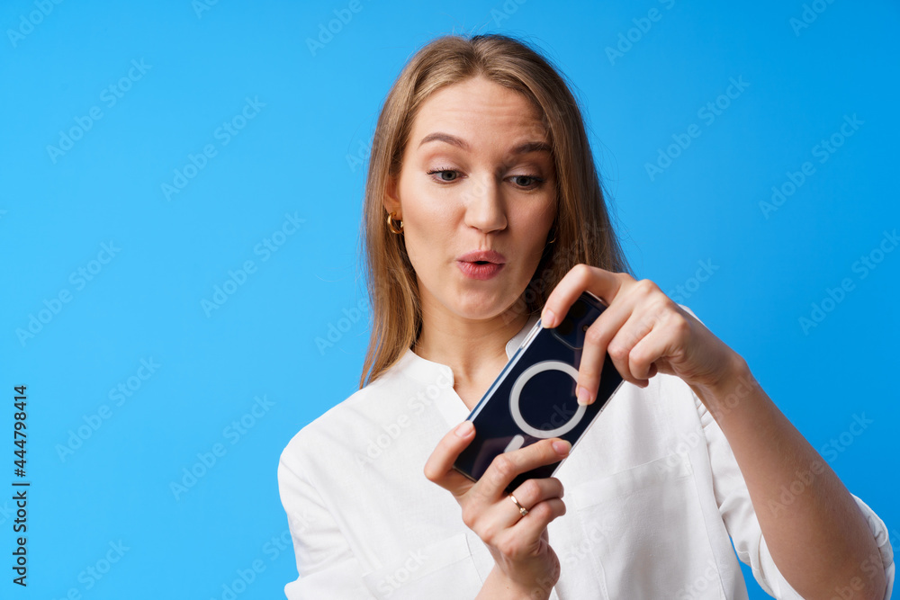 Positive young woman playing games on smartphone against blue background Positive young woman playing games on smartphone against blue background