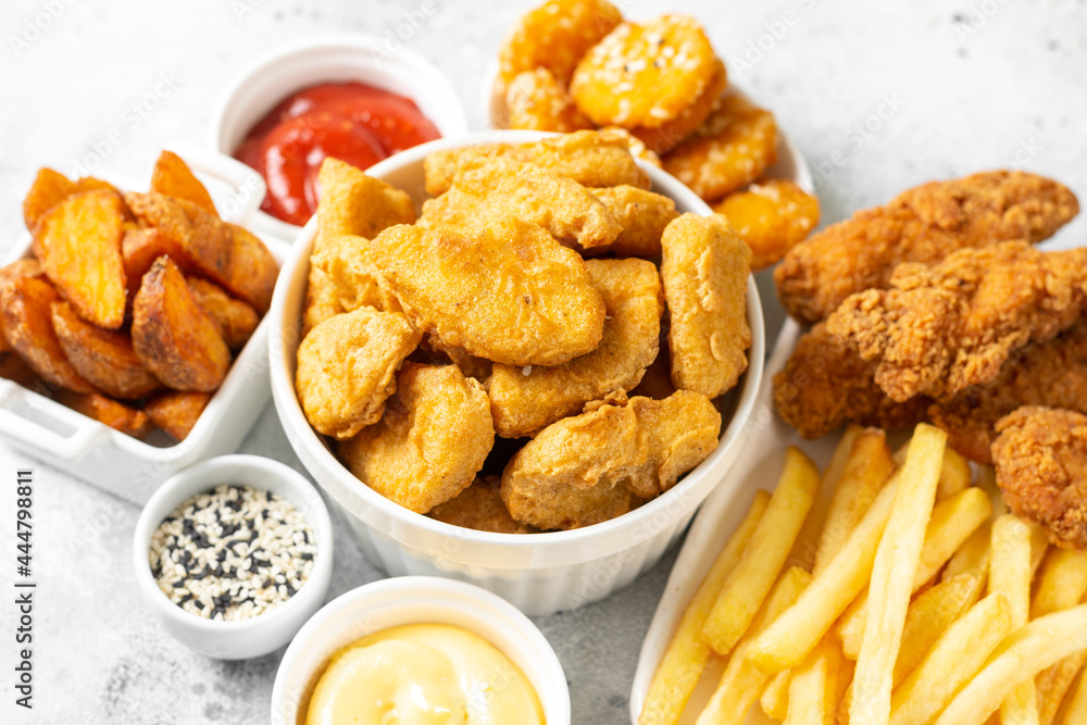 Chicken nuggets, strips, french fries, fried potatoes, ketchup and cheese sauce on a light background. Fast food closeup Chicken nuggets, strips, french fries, fried potatoes, ketchup and cheese sauce on a light background. Fast food closeup