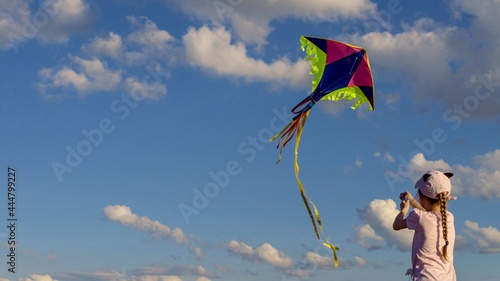 Happy child is playing with a kite. Multicolored kite on a blue sky background.