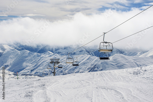 An empty chairlift on the background of snow-covered ridges tightened