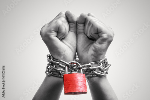 Human hands are linked by a chain with a red padlock. Black and white. Trafficking, slavery, domestic violence. Concept