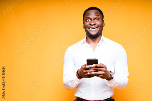 Handsome happy african american man holding phone in hand and smiling looking at camera © DmitryStock
