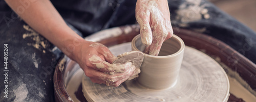 Close up female hands make dishes from clay. woman hands working on potters wheel. The master potter works in a workshop. banner