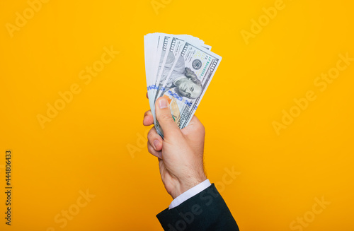 Close up photo of young male hands holding the many of dollars of USA isolated on yellow background