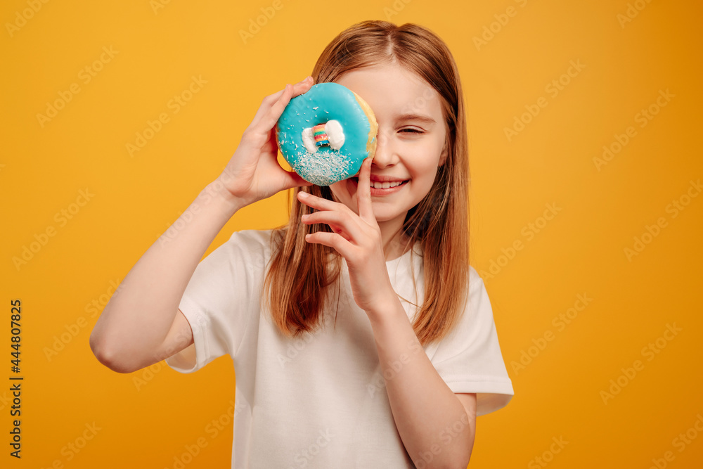 Girl child with sweet blue donut sniling isolated on yellow background with copyspace. Portrait of beautiful teen kid holding doughnut Girl child with sweet blue donut sniling isolated on yellow background with copyspace. Portrait of beautiful teen kid holding doughnut
