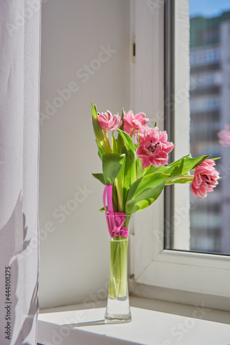 Delicate pink tulips in a vase on the windowsill on a sunny day.